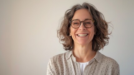 Obraz premium A portrait of a joyful mature woman with grey curly hair and glasses, smiling warmly against a soft neutral background, radiating happiness and contentment.