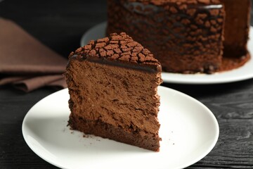 Piece of delicious chocolate truffle cake on black wooden table, closeup