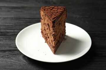 Piece of delicious chocolate truffle cake on black wooden table, closeup