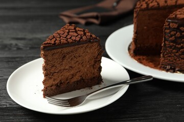 Piece of delicious chocolate truffle cake and fork on black wooden table, closeup