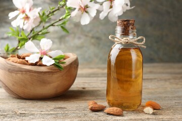 Almond oil in bottle, flowers and nuts on wooden table, closeup