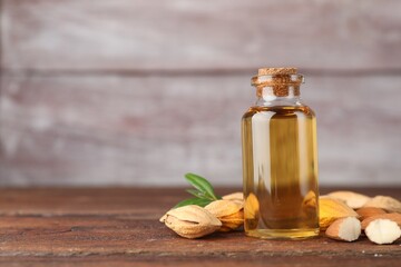 Almond oil in bottle, nuts and leaves on wooden table, closeup. Space for text