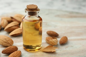 Almond oil in bottle and nuts on color marble table, closeup. Space for text