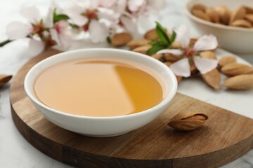 Almond oil in bowl, nuts and flowers on white table, closeup