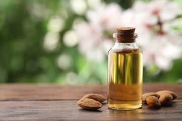 Almond oil in bottle and nuts on wooden table against blurred green background, closeup. Space for text