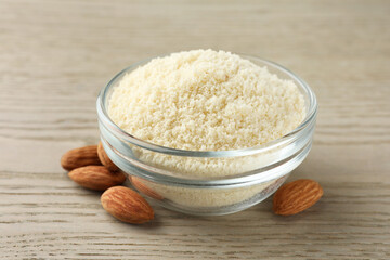 Fresh almond flour in bowl and nuts on wooden table, closeup