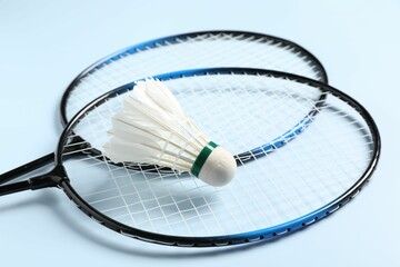 Feather badminton shuttlecock and rackets on light blue background, closeup