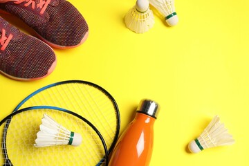 Feather badminton shuttlecocks, rackets, sneakers and bottle on yellow background, above view....