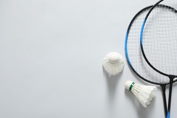 Feather badminton shuttlecocks and rackets on gray background, flat lay. Space for text