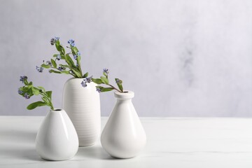 Beautiful forget-me-not flowers in vases on white marble table, closeup. Space for text