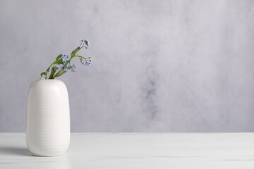 Beautiful forget-me-not flowers in vase on white marble table. Space for text