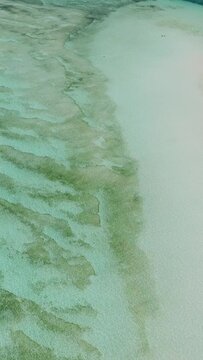 Turquoise sea water with white sand ocean floor. Sandbar with boats and waves. Surigao del Sur, Philippines. Vertical view.