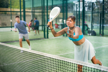 Portrait of emotional fit young woman playing padel tennis on open court in summer, swinging racket...