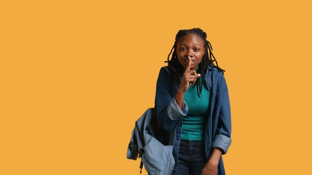 Stern african american woman doing shushing hand gesturing, irritated by noise, having negative mood. Girl placing finger on lips, doing quiet sign gesture, studio background, camera B