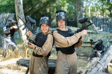 Fototapeta premium Cheerful boy and girl wearing protective paintball equipment and helmets, holding guns and posing.