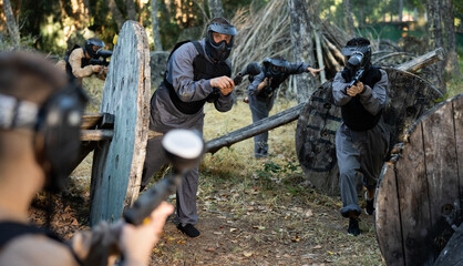 Tactical paintball team fighting on outdoor location. Men and women shooting with paintball markers.