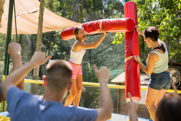 Laughing young girl fighting by soft logs with her female friend on inflatable gladiatorial arena...