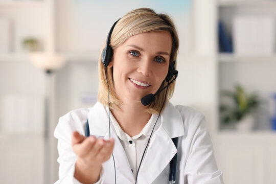 Portrait of smiling doctor in headphones having online consultation indoors