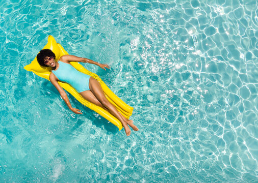 Young biracial woman enjoys a relaxing day on a pool float, with copy space - Powered by Adobe