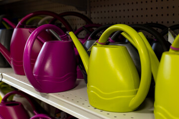 Selective focus of selection of plastic watering cans in magenta and yellow-green colours on store shelf