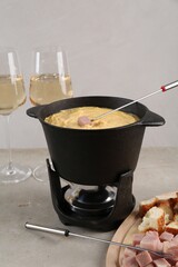 Fondue pot with tasty melted cheese, forks, wine and different snacks on white table