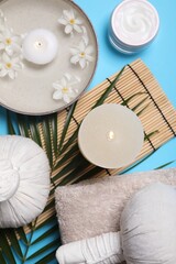 Flat lay composition with spa products, burning candle and beautiful flowers on light blue background