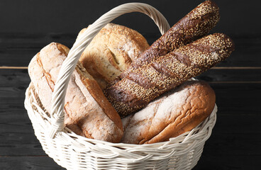 Wicker basket with different types of fresh bread on black wooden table