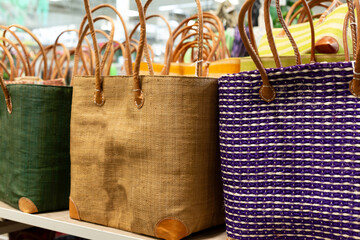 Selective focus of row of straw and burlap shopping bags with faux leather handles set on shelves for sale