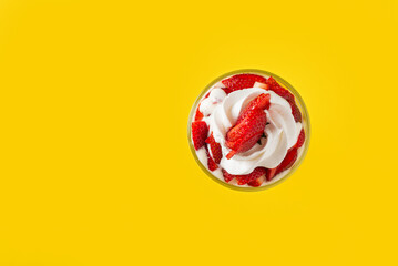 Strawberries with cream in a glass cup, on yellow background. Top view. Copy space.