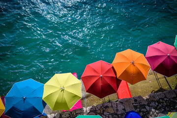 A cluster of vibrant umbrellas dotting the shoreline, providing shade on a hot summer day. - Powered by Adobe