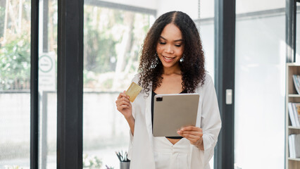 Businesswoman holds a credit card and reads from a tablet in a well-lit office, preparing for a financial transaction.