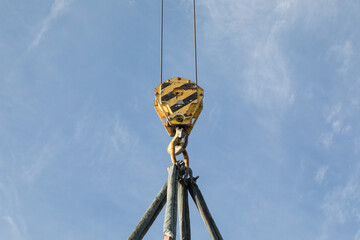the hook of a crane with a lifting bridle hanging down from a boom on a clear sky © SockaGPhoto