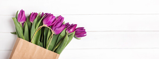 Purple tulips in paper bag on the white wooden table, spring background