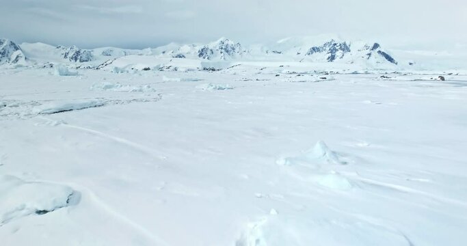 Fly above frozen panorama of Antarctic Peninsula. Desert white land of snow mountains and ice drone shot. Antarctica travel exploration. Discover beauty of South Pole. Wild nature winter background