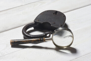 Old padlock and magnifying glass on the wooden desk table background. Secret information concept....