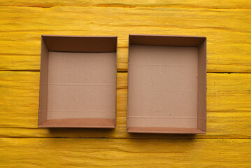 Open empty cardboard boxes on the yellow wooden flat lay desk table background.