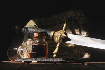Magic potion bottle and sword on the old wooden table background front view. Witchcraft concept.
