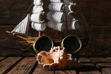 Sea travel concept background. Pirate ship, binoculars and seashell on the old table background...