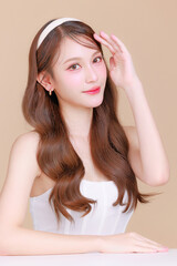 Pretty Asian beauty woman curly long hair with Korean makeup glowing face and healthy facial skin portrait smile on isolated beige background. Cosmetology ,Plastic surgery.