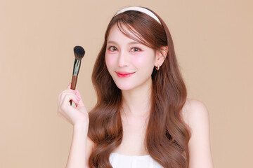 Pretty Asian beauty woman curly long hair holding brush with Korean makeup glowing face and healthy facial skin portrait smile on isolated beige background. Cosmetology ,Plastic surgery.
