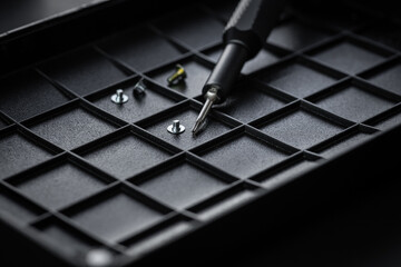 Torx drive bit and aluminum bit driver on black sorting tray. Screws and drive bits. Screwdriver handle with magnetic bit socket and knurled grip.
