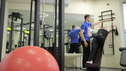 Man assisting woman with knee exercises in gym for physical fitness