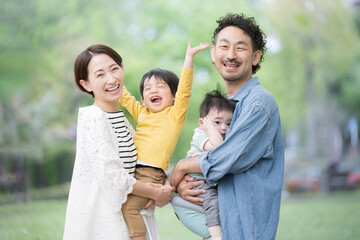 メインビジュアルにも！逆光の新緑の公園で遊ぶ仲良しで笑顔の日本人家族　カメラ目線　上半身のクローズアップ