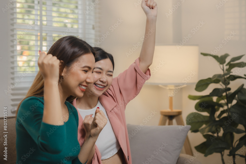 Wall mural two beautiful asian teenage girls are having fun watching entertainment together at home on the sofa