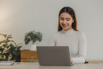 A beautiful Asian woman is sitting and working in her home office, A female employee is working by wirelessly connecting to a colleague at her own home.