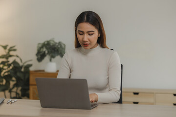 A beautiful Asian woman is sitting and working in her home office, A female employee is working by wirelessly connecting to a colleague at her own home.