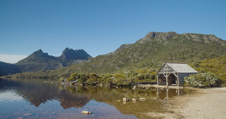 the old boat shed at dove lake with cradle mt in the distance on a calm summer morning at cradle mountain national park