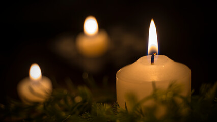 A large candle in focus and two candles in the background of the image. Three candles lit in the...