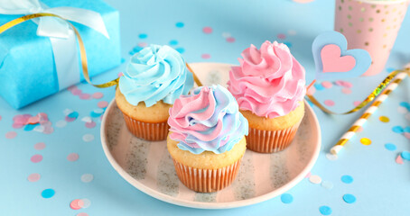 Plate with delicious cupcakes, gift box and decorations on blue background. Gender reveal party concept