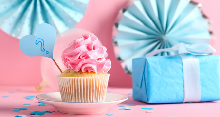 Delicious cupcake with question mark, gift box and decorations on pink background. Gender reveal party concept